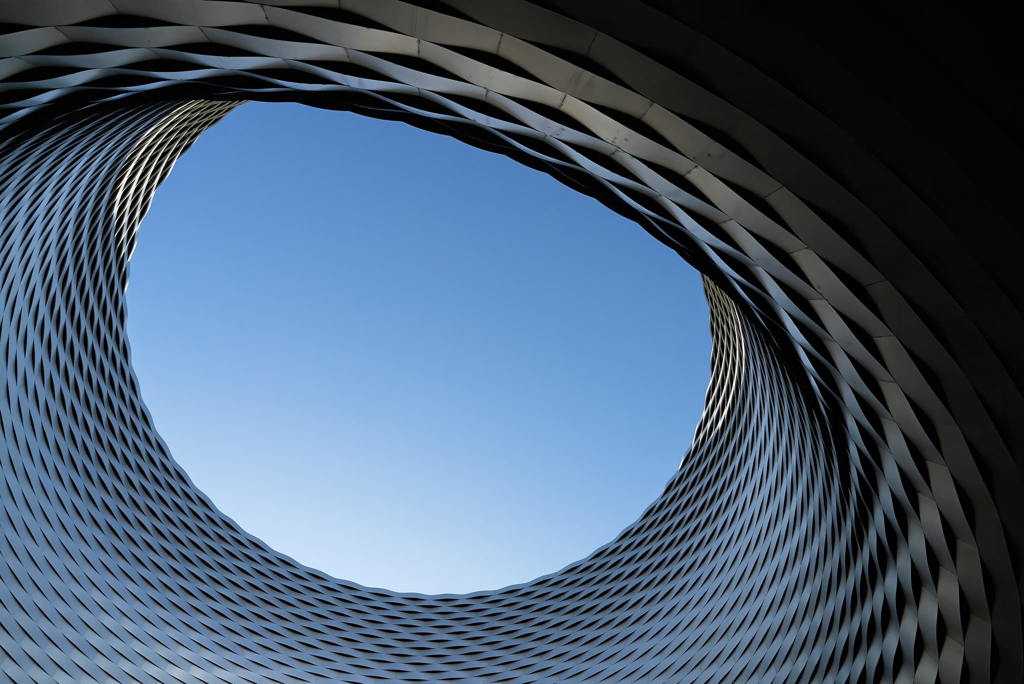 Facciata architettonica in metallo intrecciato con un'apertura circolare verso il cielo
